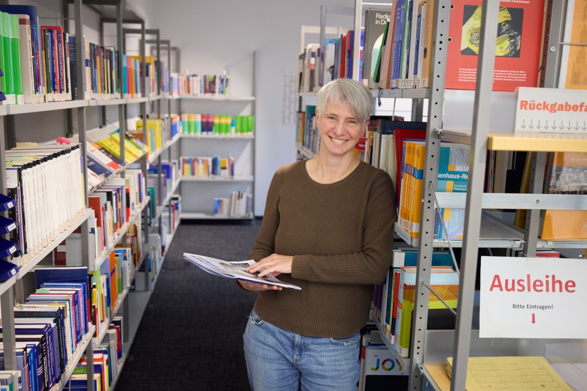 An IQWiG employee stands in the library with a journal in her hands